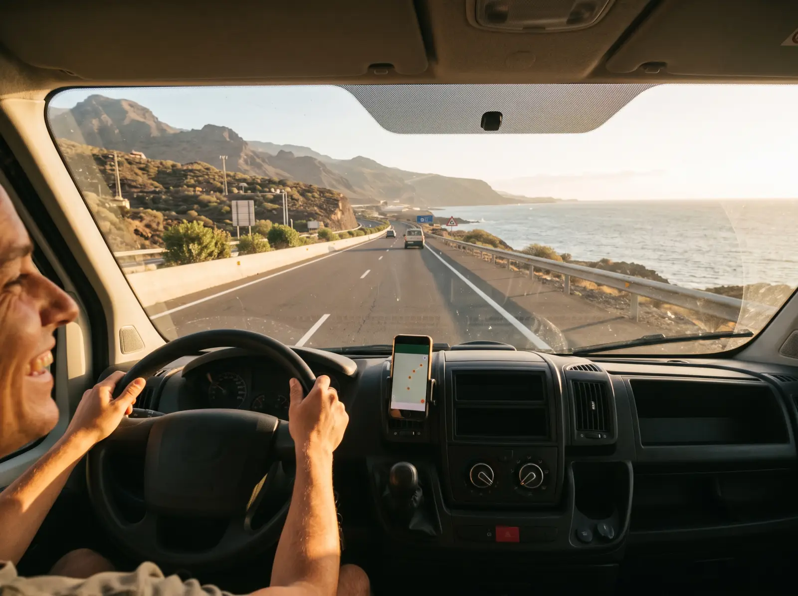 A van driver on a coast road with a phone in a dashboard mount showing a map.